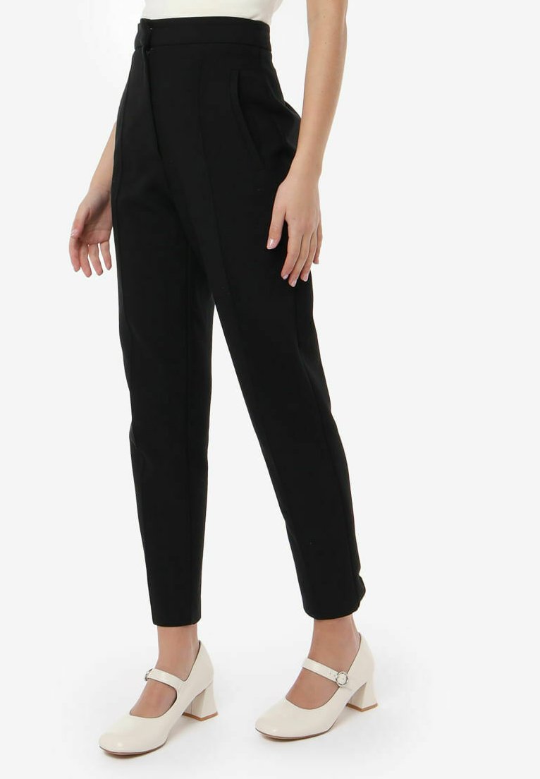 Pantalones negros ajustados de talle alto, con tejido suave, bolsillos laterales y una silueta ceñida, combinados con zapatos blancos de tacón bloque.