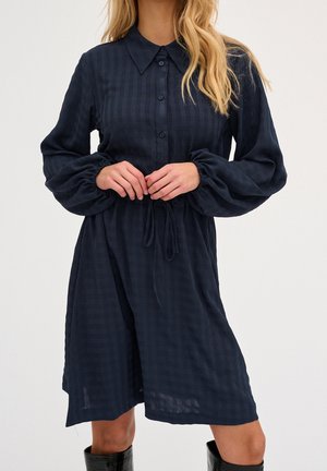 Marineblaues Kleid aus leichtem Stoff mit Kragen, Knopfleiste vorne, langen Puffärmeln und Kordelzug in der Taille. Strukturmuster sichtbar.