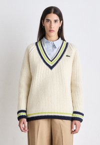 Cremfarbener Strickpullover mit V-Ausschnitt, der marineblau und limettengrüne gestreifte Akzente, gerippte Bündchen und ein Lacoste-Logo auf der Brust aufweist.
