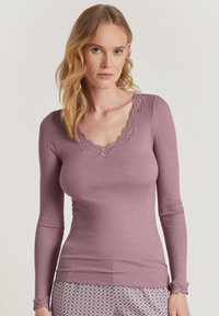 Langsleeve, ribbel top in gedempt lavendel met een golvende kant V-halslijn en kantaccenten bij de manchet. Gladde textuur.