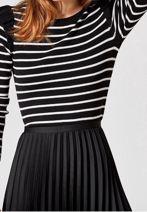 Svart och vit randig långärmad topp i kombination med en plisserad svart kjol med en slät midja och vertikal textur.