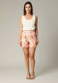 Top en maille blanche associé à un short à motifs rose et orange avec une taille élastique. Le modèle porte des sandales plates.