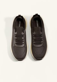 Zwarte sport sneakers met mesh stof, textuur oppervlak, ronde neus, gevoerde kraag en contrasterende lichtgekleurde zool. Veters centraal gepositioneerd.