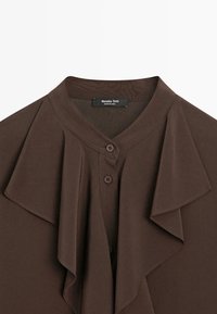 Blouse marron avec encolure ronde, détail volanté sur le devant et trois boutons centraux, étiquette Massimo Dutti.
