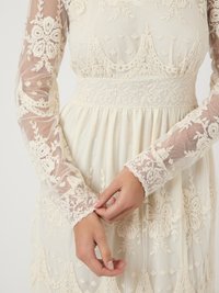 Vestido de encaje con un diseño de mangas largas y transparentes. Presenta intrincados bordados florales, un corpiño ajustado y una falda acampanada en color crema.