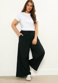 Pantaloni a palazzo a righe nere realizzati in tessuto leggero, dotati di una vita elasticizzata con un cordino. Indossati con una maglietta bianca semplice e sneakers.