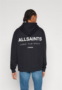 Fekete kapucnis pulóver, nagy fehér betűkkel "ALLSAINTS" felirattal és japán karakterekkel a hátsó részén. Puha anyagból készült, hosszú ujjú.