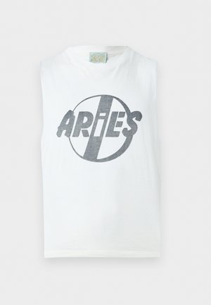 Mężczyzna ubrany w białą koszulkę bez rękawów z logo "ARIES", czarne szerokie spodnie, brązowe buty i czarne okulary przeciwsłoneczne, stojący na białym tle.