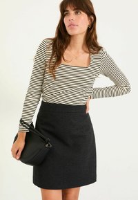 Gestreiftes Langarmoberteil in Schwarz und Weiß, kombiniert mit einem schwarzen strukturierten Rock, accessorisiert mit einer kleinen schwarzen Handtasche.