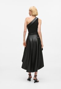 Μαύρη δερμάτινη τοπ με έναν ώμο, με εφαρμοστό μπούστο, ρέουσα φούστα, ασύμμετρο σχέδιο και λεπτομέρεια πλευρικής τσέπης.