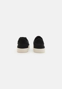 Svart ruskinnsneakers med en teksturert overflate, polstret krage og en hvit gummisåle. Har et strømlinjeformet design og minimalistisk stil.