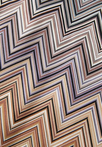 Nærbilde av stoff med et gjentakende zigzag-mønster i nyanser av brunt, beige, grått og svart som danner nestede chevroner.