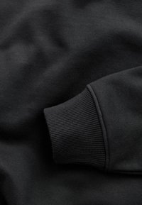 Fekete kapucnis pulóver anyag sima textúrával és bordázott mandzsetta részletekkel; puha, matt felülettel és enyhén rugalmas nyakkivágással rendelkezik.