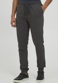 Grey sweatpants made of soft fabric, featuring a drawstring waist, tapered legs, and side pockets, paired with black sneakers.