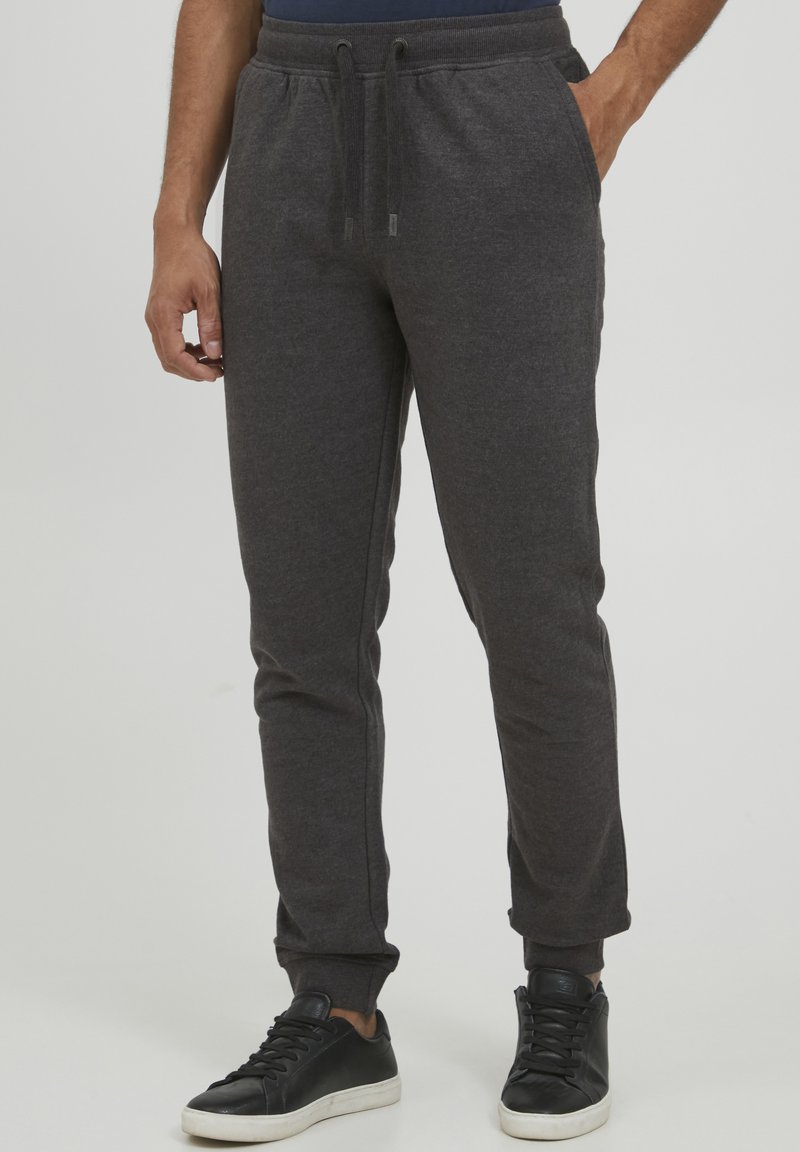 Grå joggebukser laget av mykt stoff, med snøring i livet, tapered ben og sidelommer, sammen med svarte joggesko.