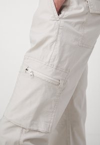 Vaaleanbeiget cargo-housut, jotka on valmistettu pehmeästä ja kestävästä kankaasta. Niissä on vetoketjullinen tasku reisiosassa ja rento istuvuus.