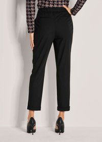 Zwarte tapered broek met een elastische tailleband, voorzien van opgerolde boorden en zijzakken. Gladde textuur, gecombineerd met hoge zwarte hakken.