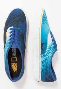 Sneakers in tela blu con design a onda dell'oceano, accenti scuri e accessori gialli. Suola in gomma bianca con una soletta decorata.