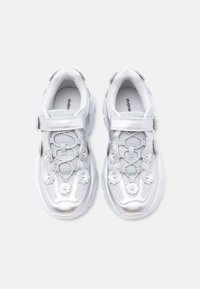 Baskets blanches de sport avec des accents en mesh et synthétique brillant. Elles comportent une bride Velcro, des ornements floraux et une semelle en caoutchouc épaisse.