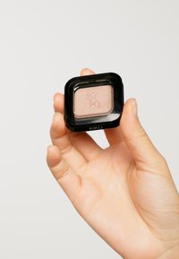 KIKO oogschaduw in een vierkante zwarte compactsdoos, vastgehouden in een hand, met een lichtbeige kleur en een subtiele shimmerafwerking, en een gegraveerd logo.