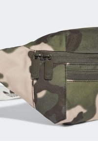 Kamouflage-mönstrad tygpåse med två mörka dragkedjor och en framficka med dragkedja, som visar detaljerad sömnad och textur.