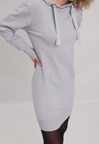 Robe à capuche grise en tissu doux, dotée d'une capuche avec cordon de serrage, de manches longues et de poignets et ourlet côtelés. Design minimaliste.