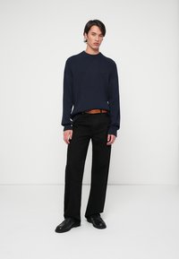 Sweater de malha em azul-marinho, calças pretas de corte relaxado, cinto castanho e sapatos pretos. Design minimalista com uma silhueta clássica.