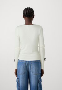 Maglietta bianca a maniche lunghe con texture a coste, con accenti neri sulle maniche, abbinata a pantaloni cargo in denim blu con tasche.