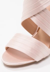 Sandale à talon haut en satin rose ouvert à l’avant, avec deux larges brides croisées sur le pied et une semelle intérieure rembourrée.
