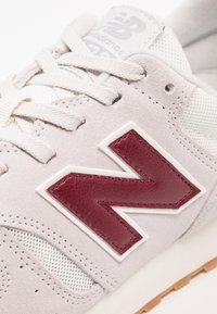 Baskets gris clair avec panneaux en mesh blanc et un accent en cuir bordeaux. Dispose de lacets ronds et d'une semelle en caoutchouc. Design minimaliste.