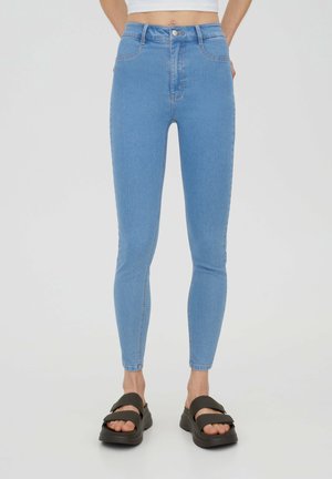 Jeans skinny taille haute bleu clair en denim. Présente cinq poches, un bouton de fermeture à l'avant et une coupe élégante jusqu'aux chevilles.