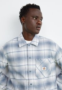 Camicia a scacchi button-up in flanella blu chiaro e bianco, con tasca frontale con etichetta, colletto alla francese e tessuto testurizzato.