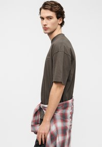 Σκούρο γκρι βαμβακερό T-shirt με κοντά μανίκια και στρογγυλή λαιμόκοψη, συνδυασμένο με κόκκινο και γκρι καρό πουκάμισο δεμένο στη μέση.