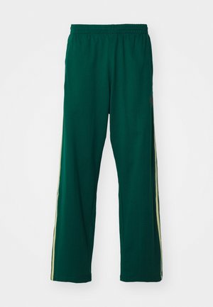Pantalon de sport vert foncé avec une ceinture élastique et des bandes claires courant le long des côtés extérieurs des deux jambes.
