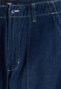 Pantalones de mezclilla azul oscuro con cierre de botón, costuras blancas en contraste y una cintura estándar. Presenta un diseño de corte recto, sin patrones.