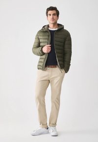 Oliwkowa pikowana kurtka z kapturem, zapinana na zamek, z przeszyciami. Połączona z beżowymi spodniami i białymi tenisówkami. Pod spodem gładka czarna koszulka.