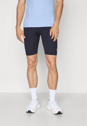 Men's athletic outfit featuring a light blue fitted top and snug navy shorts, paired with white sneakers and ankle-length socks.