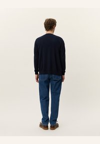 Cardigan lavorato a maglia blu scuro con maniche lunghe, polsini e orlo a coste, abbinato a jeans blu dritti e scarpe marroni. Tessuto testurizzato.