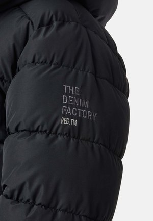 Schwarze Steppjacke mit gestepptem Design. Auf der linken Schulter steht "THE DENIM FACTORY" in gestickten silbernen Buchstaben.
