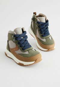 Baskets montantes vertes et beiges avec des panneaux en maille, un bout renforcé, des lacets bleus et une semelle blanche épaisse, présentant des accents marron et des zips sur le côté.