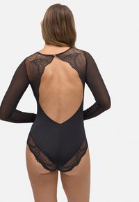 Body negro con mangas largas transparentes, diseño de espalda abierta, detalles de encaje en los hombros y el dobladillo, y una silueta ajustada.