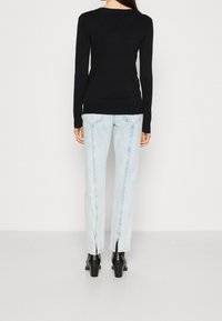 Zwarte lange mouwen top met een ronde hals, gecombineerd met lichtblauwe rechte jeans, met splitte zomen en zwarte haklaarzen.