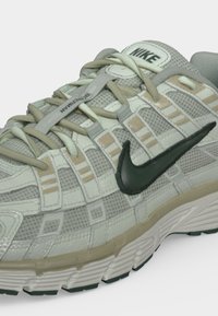Γκρι και μπεζ αθλητικό παπούτσι Nike για τρέξιμο με πλεκτό πάνω μέρος, μαύρο λογότυπο Swoosh και μπεζ κορδόνια δεμένα μπροστά.