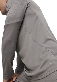 Graues Sport-Langarmshirt mit strukturierten Mustern an den Schultern, hergestellt aus leichtem, feuchtigkeitsableitendem Material, mit einem DRYCELL-Logo.