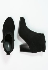 Czarne zamszowe botki do kostki na słupku, z zamkiem błyskawicznym z boku i spiczastym noskiem dla eleganckiego wyglądu.