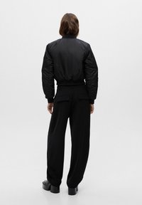 Chaqueta bomber negra con un acabado texturizado, puños y dobladillo elásticos, combinada con pantalones de pierna ancha, ambos en un corte relajado. Calzado de plataforma negro.