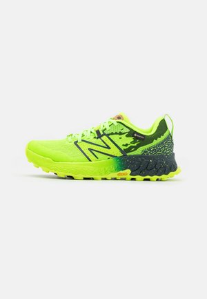 Hellgrüner und schwarzer Sportschuh mit Schnürsenkeln, strukturierter Sohle und New Balance-Logo an der Seite vor weißem Hintergrund.