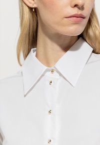 White button-up shirt with a structured collar, featuring golden buttons and a smooth texture. Includes a subtle sheen.