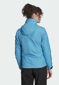 Blauwe waterdichte jas met een aansluitend ontwerp, verstelbare capuchon en elastische manchetten. Glad textuur met een lichtgewicht, ademend stof.