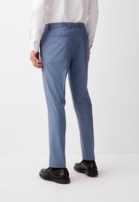 Light blue dress pants made of a fine-textured fabric, tailored fit, with back pockets and worn with black dress shoes.